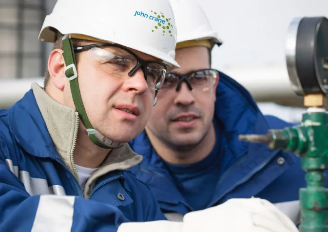 Two men in hard hats and safety glasses working on a gas valve